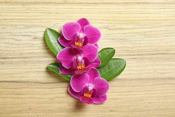 Top view of beautiful orchid flowers with green leaves on wooden background