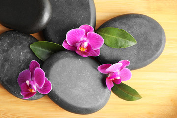 Spa stones and orchid flowers on wooden background, top view