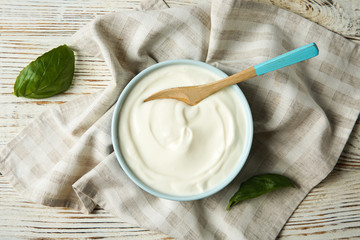Bowl of sour cream with spoon and napkin on white wooden table, flat lay