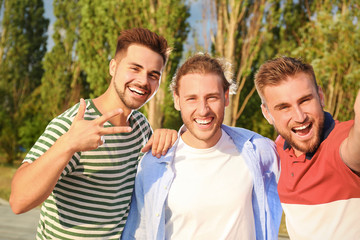 Happy young men taking selfie outdoors on sunny day