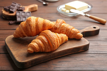 Board with tasty croissants on wooden table. French pastry