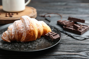 Plate of tasty croissant with powdered sugar and chocolate on dark wooden table. French pastry