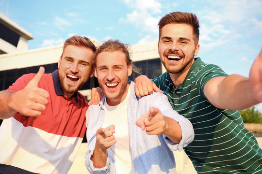 Happy young men taking selfie outdoors on sunny day