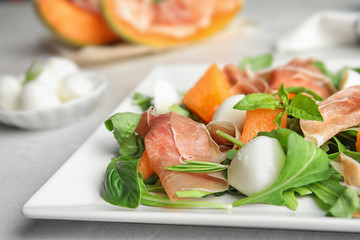 Fresh melon with prosciutto, mozzarella and arugula on plate, closeup