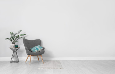 Stylish room interior with comfortable armchair and plant near white wall. Space for text