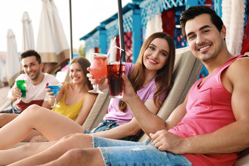 Happy young friends with fresh summer cocktails relaxing on sunbeds