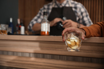 Young man with glass of whiskey in bar, closeup. Space for text
