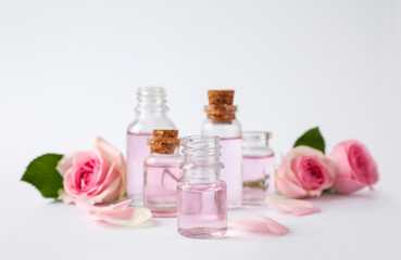 Fototapeta na wymiar Bottles of essential oil and roses on white background