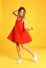 Beautiful young woman in red dress dancing on yellow background