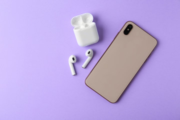 Wireless earphones, mobile phone and charging case on violet background, flat lay. Space for text