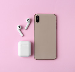 Wireless earphones, mobile phone and charging case on pink background, flat lay