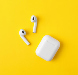 Modern wireless earphones and charging case on yellow background, flat lay
