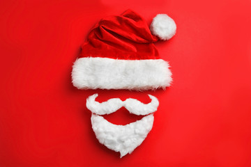 Obraz na płótnie Canvas Santa Claus hat with white beard on red background, flat lay