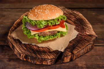 Tasty grilled homemade burger with beef, tomato, cheese, cucumber and lettuce. Delicious grilled burgers. Craft beef burger and french fries on wooden table.