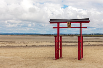 Red torii gate on strand near Mont Saint-Michel abbey on tidal island. Normandie, Nothern France