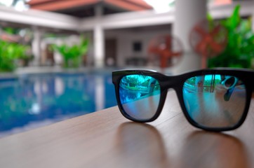 Blue sunglasses are placed on a poolside table. Summer holiday view.