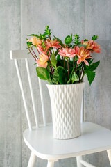 Bouquet of dahlia flowers in ceramic vase, standing on white wooden chair