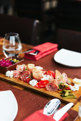 Cold cuts on wooden board with prosciutto, bacon, salami and sausages. Meat platter appetizers served with pickle and olives on dining table with cutlery.