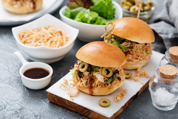 Pulled chicken sandwiches with barbeque sauce and lettuce on light blue or gray background.