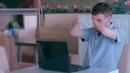 Problem adaptation to life people with disabilities. Independent handicapped young guy. Tired disabled man with amputated two stump hands in cafe works types on laptop. Freelancer computer online job.