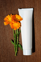 Pot Marigold (Calendula officinalis) with cream in a tube on a wooden board. Orange flowering medicinal plant of the family Asteraceae.