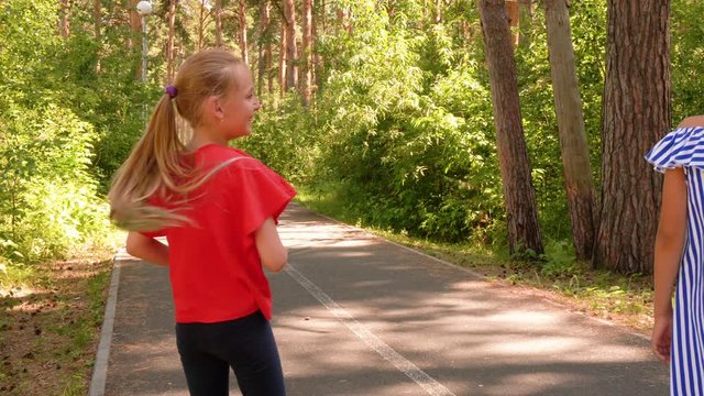 Happy childhood and outdoor activities at summer vacations. Teen girls throw fir cones playing the game together in nature park. Friends ae standing on asphalt walkway. Walking in park.