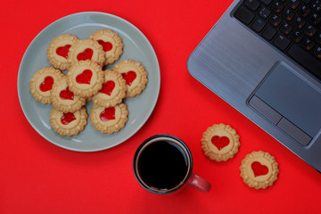 Heart shaped red jam filled cookies and a cup of coffee with laptop on red background.Valentines day concept