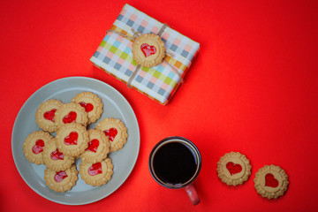 Heart shaped red jam filled cookies and a cup of coffee with laptop on red background.Valentines day concept