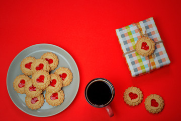 Heart shaped red jam filled cookies and a cup of coffee with laptop on red background.Valentines day concept