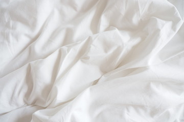 Closeup of beautiful white shiny crumpled polyester fabric sheets on the bed with warm motion and...