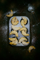 Homemade cookies in baking tray on dark background with powedered sugar
