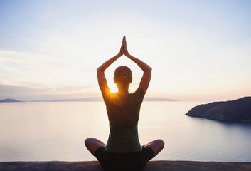 Jonge vrouw die yoga beoefent in de buurt van de zee bij zonsondergang. Harmonie, meditatie, gezonde levensstijl, ontspanning, yoga, zelfzorg, mindfulness concept