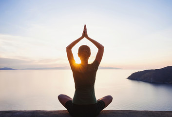 Young woman practicing yoga near the sea at sunset. Harmony, meditation, healthy lifestyle, relaxation, yoga, self care, mindfulness concept - obrazy, fototapety, plakaty