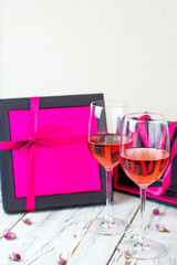 Two glasses of rose wine on white wooden table with pink gift boxes on background