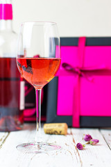 Two glasses of rose wine on white wooden table with pink gift boxes on background