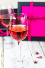 Two glasses of rose wine on white wooden table with pink gift boxes on background