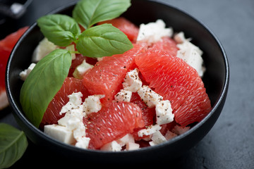 Close-up of salad with grapefruit, feta cheese and green basil in a black bowl, selective focus