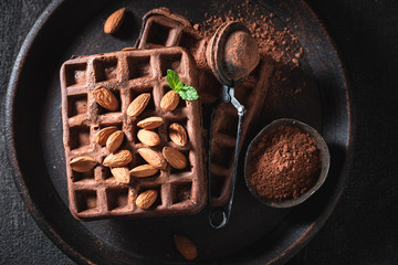 Delicious waffles made of chocolate and nuts on dark table