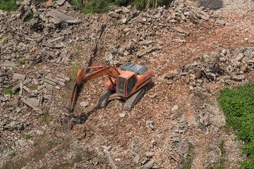 Orange large excavator in the field work impact broken stone aerial shot top view
