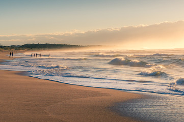 Ocean beach at sunrise with unrecognizable people doing sports