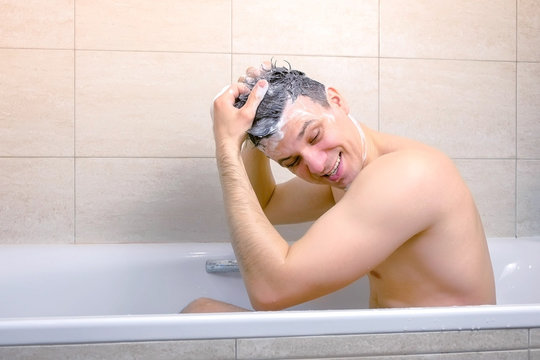 Man Is Washing His Head With Shampoo And Making A Mohawk From Hairs Sitting In Bathtub. Side View.