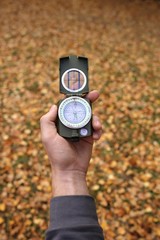 Naklejka premium Autumn concept. Autumn travel.Compass in a hand on a background of brown foliage 