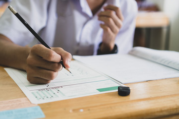 School / university Students hands taking exams, writing examination room with holding pencil on optical form answers paper sheet on desk doing final test in classroom. Education assessment Concept