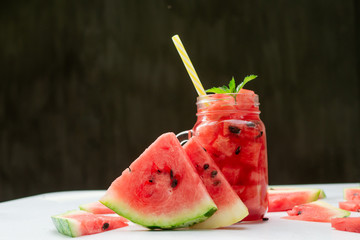 Summer watermelon drink in glass and slices of watermelon on dark background