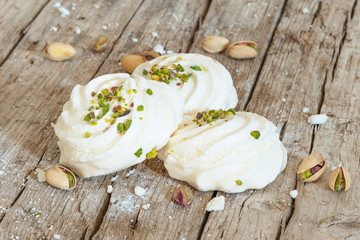 White marshmallows on old wooden background decorated with pistachios. Front view.