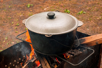 Open air kitchen at party picnic. Pilaf cooking on fire outdoor. Big pot closed with cover stays on wire rack and steams. Close up image of meal dish preparation