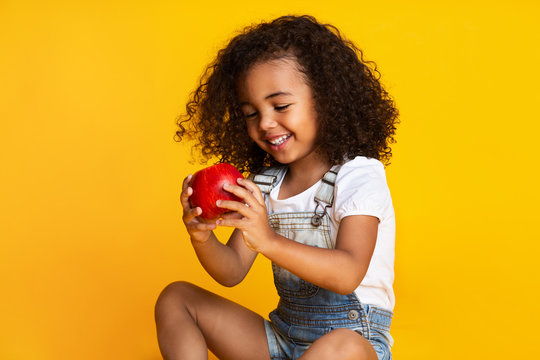 Pretty girl holding red apple over yellow studio background