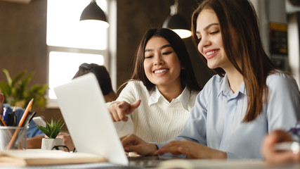 Happy student girls doing project together on laptop