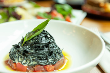 Black spaghetti with fish in a plate. Decorated with basil leaf. Close-up.