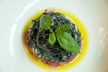 Black spaghetti with fish in a plate. Decorated with basil leaf. Top view. Close-up.